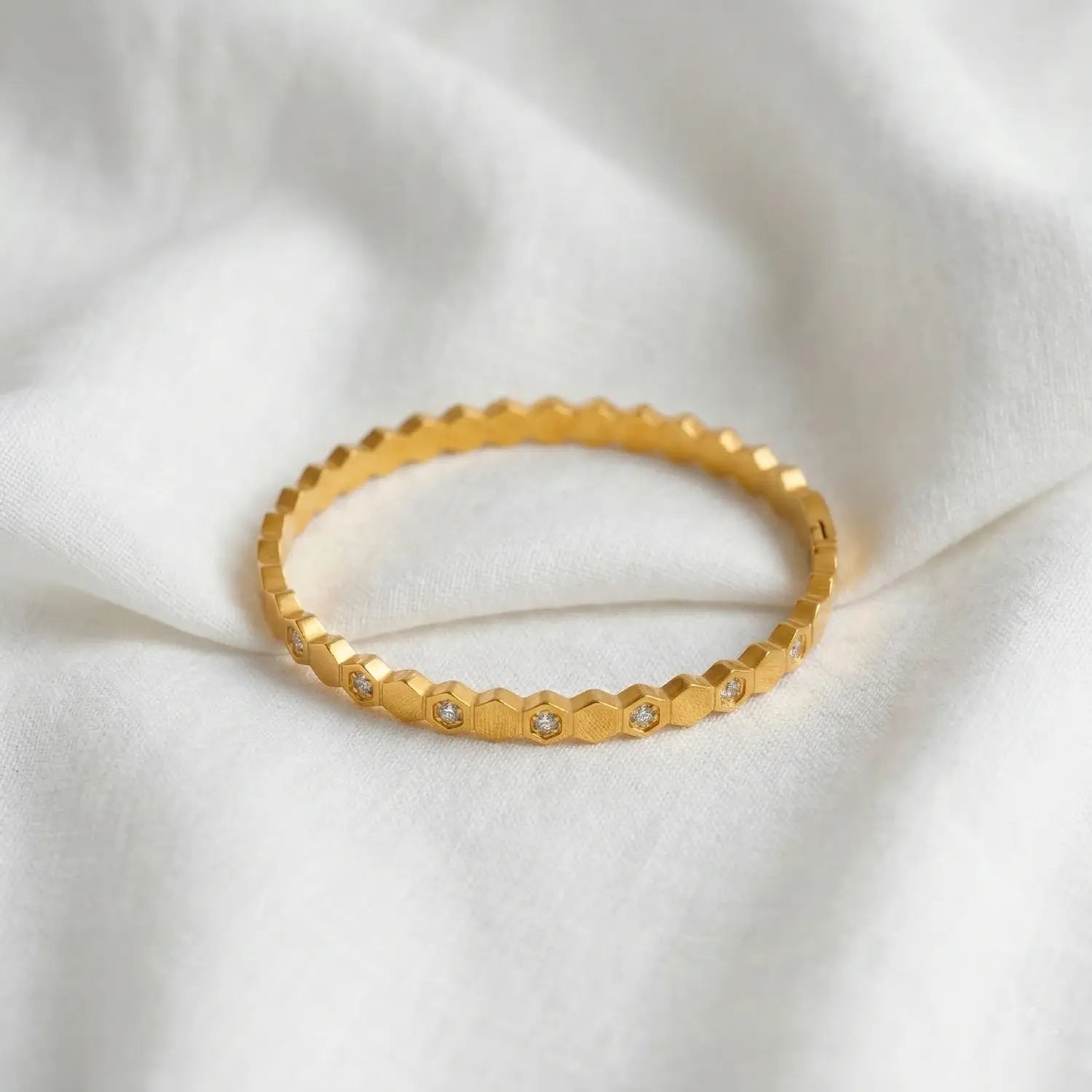 Gold bracelet with hexagonal pattern and small stones on a white fabric background