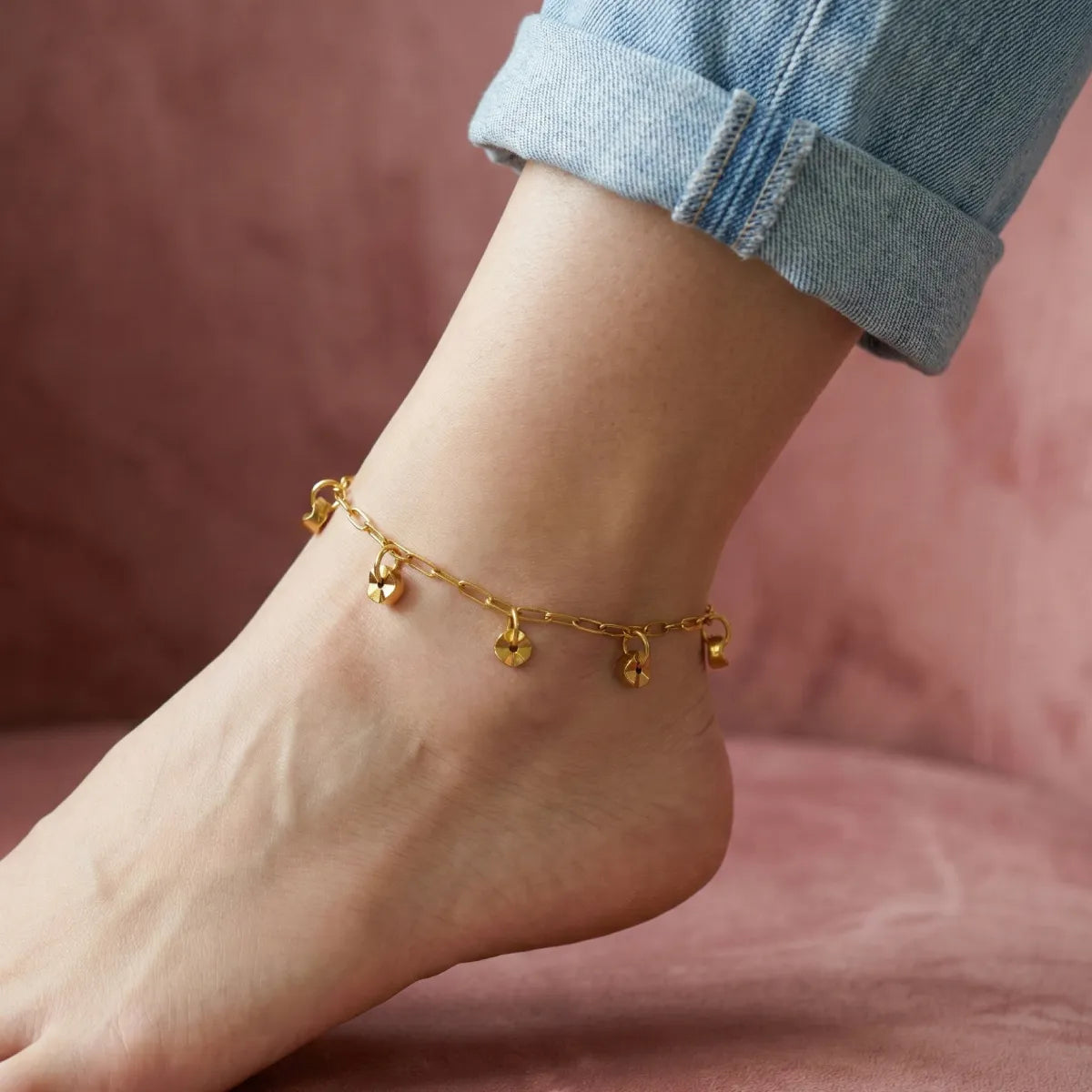 Gold anklet on a foot with a blurred pink background