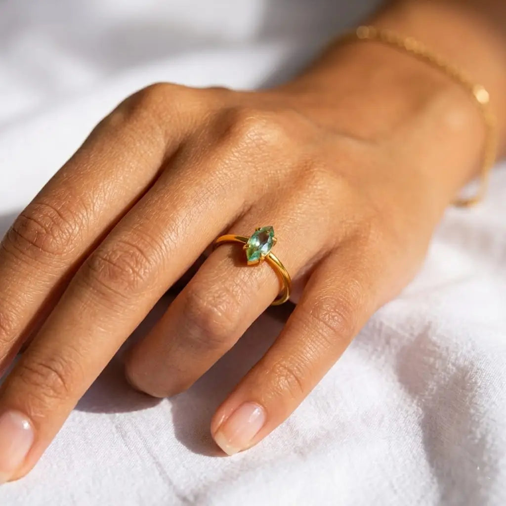 Hand wearing a gold ring with a green gemstone on a white background