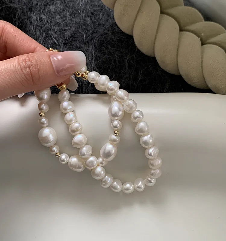 Pearl hoop earrings held by a hand on a white surface with a blurred background