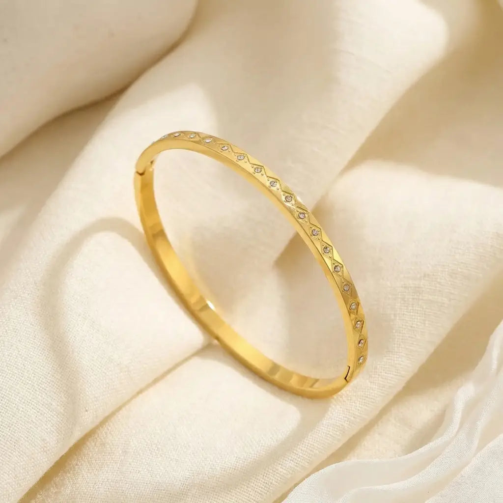 Gold bracelet with small stones on a soft beige fabric background