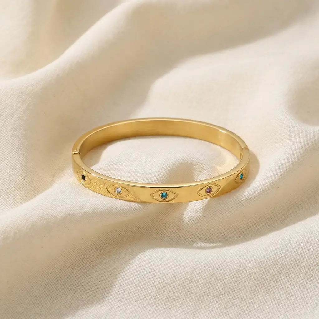 Gold bracelet with embedded stones on a beige fabric background