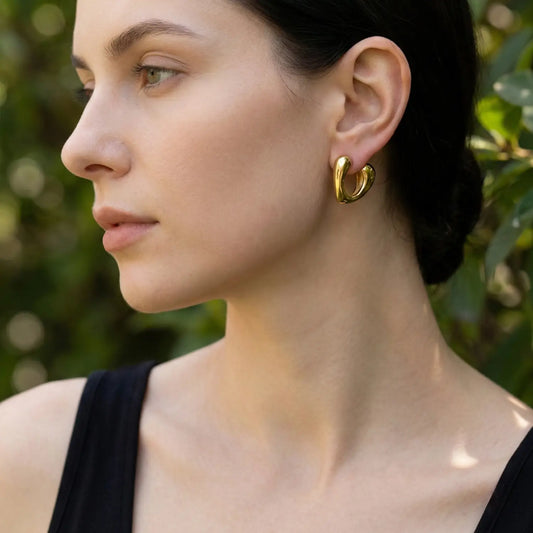 Woman wearing a gold hoop earring with a blurred green background