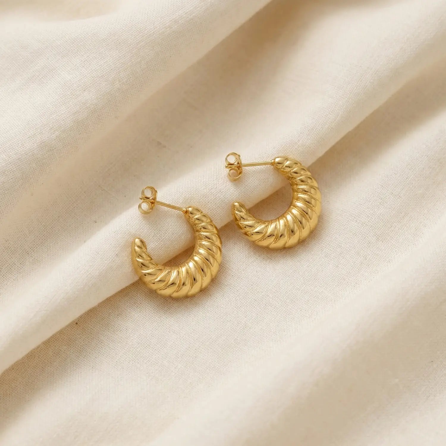 Gold hoop earrings on a beige fabric background