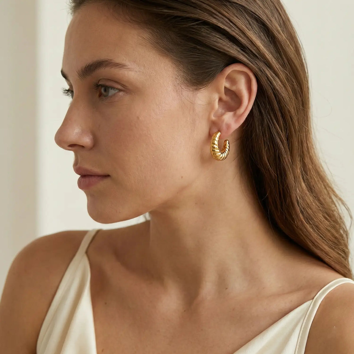 Woman wearing gold hoop earrings with a neutral background