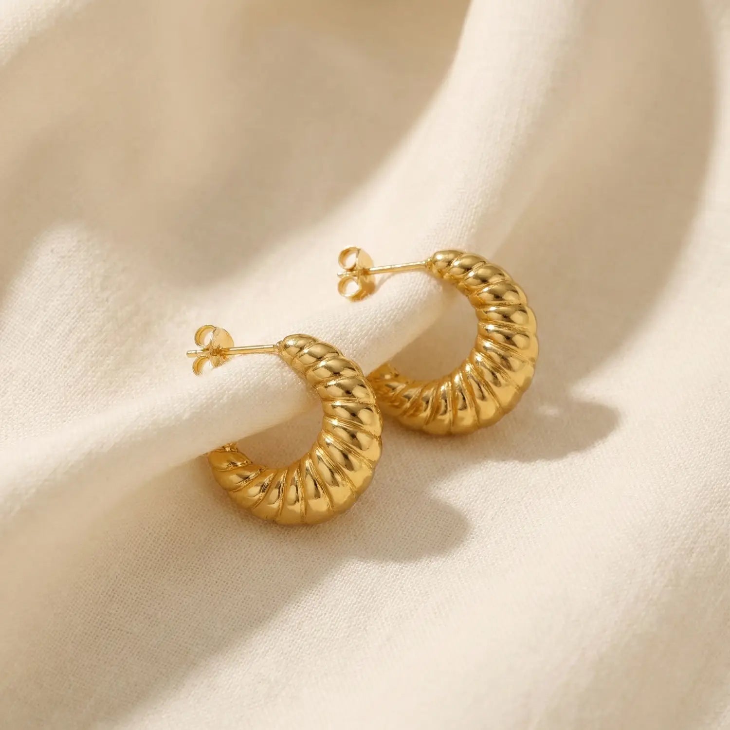 Gold hoop earrings on a beige fabric background