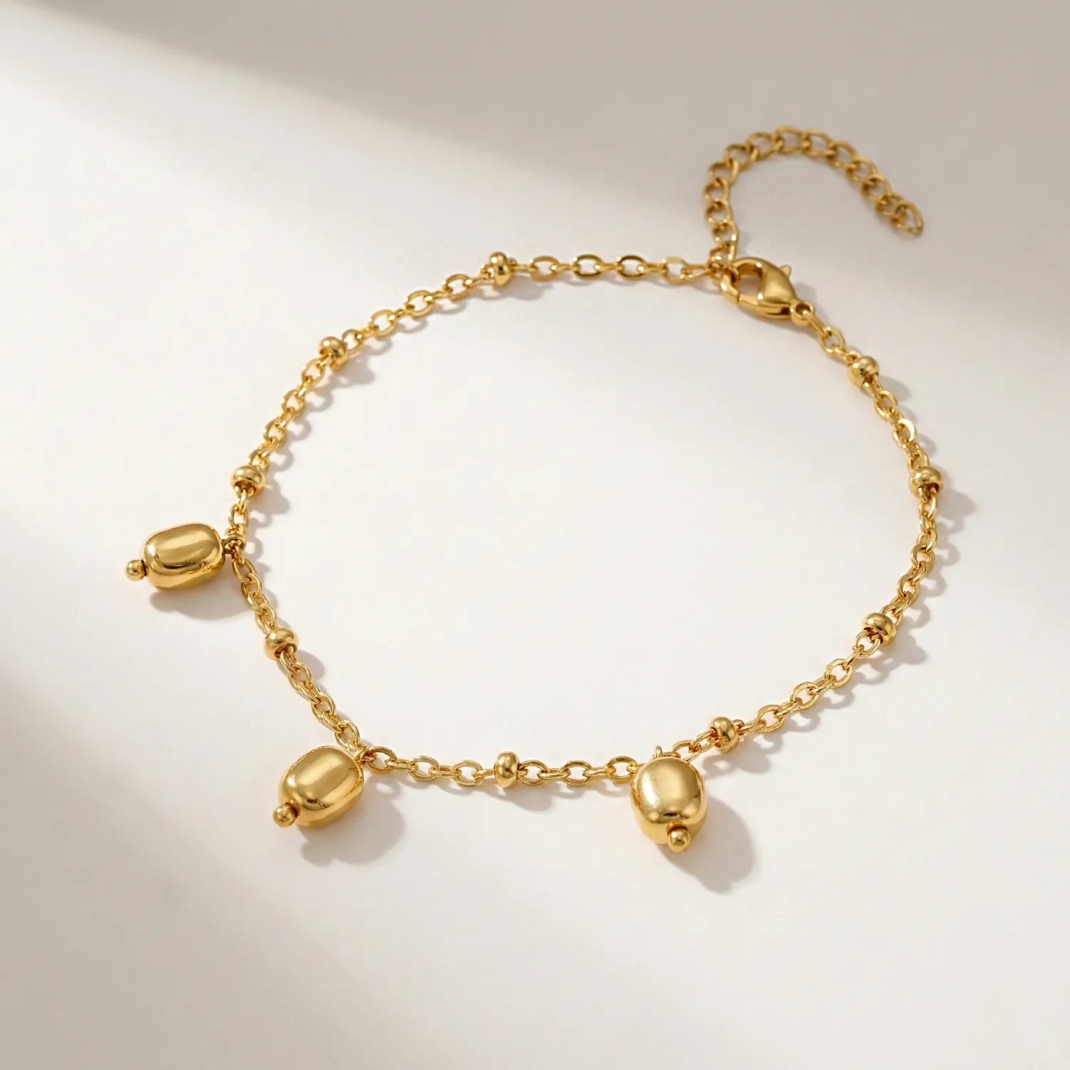 Gold bracelet with three heart-shaped charms on a light background