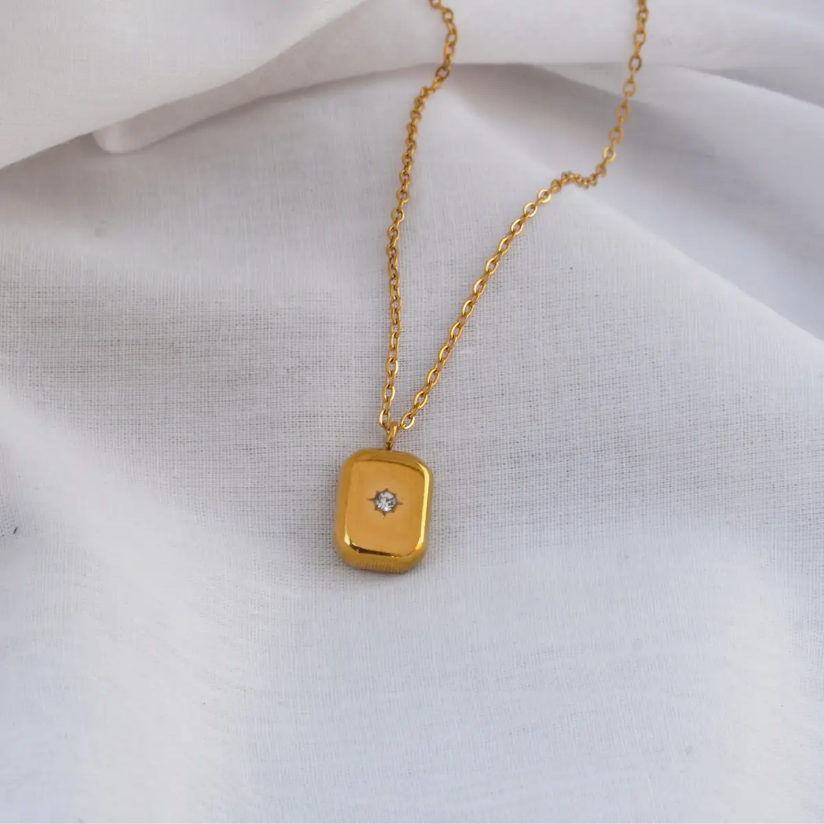 Gold necklace with a rectangular pendant on a white fabric background