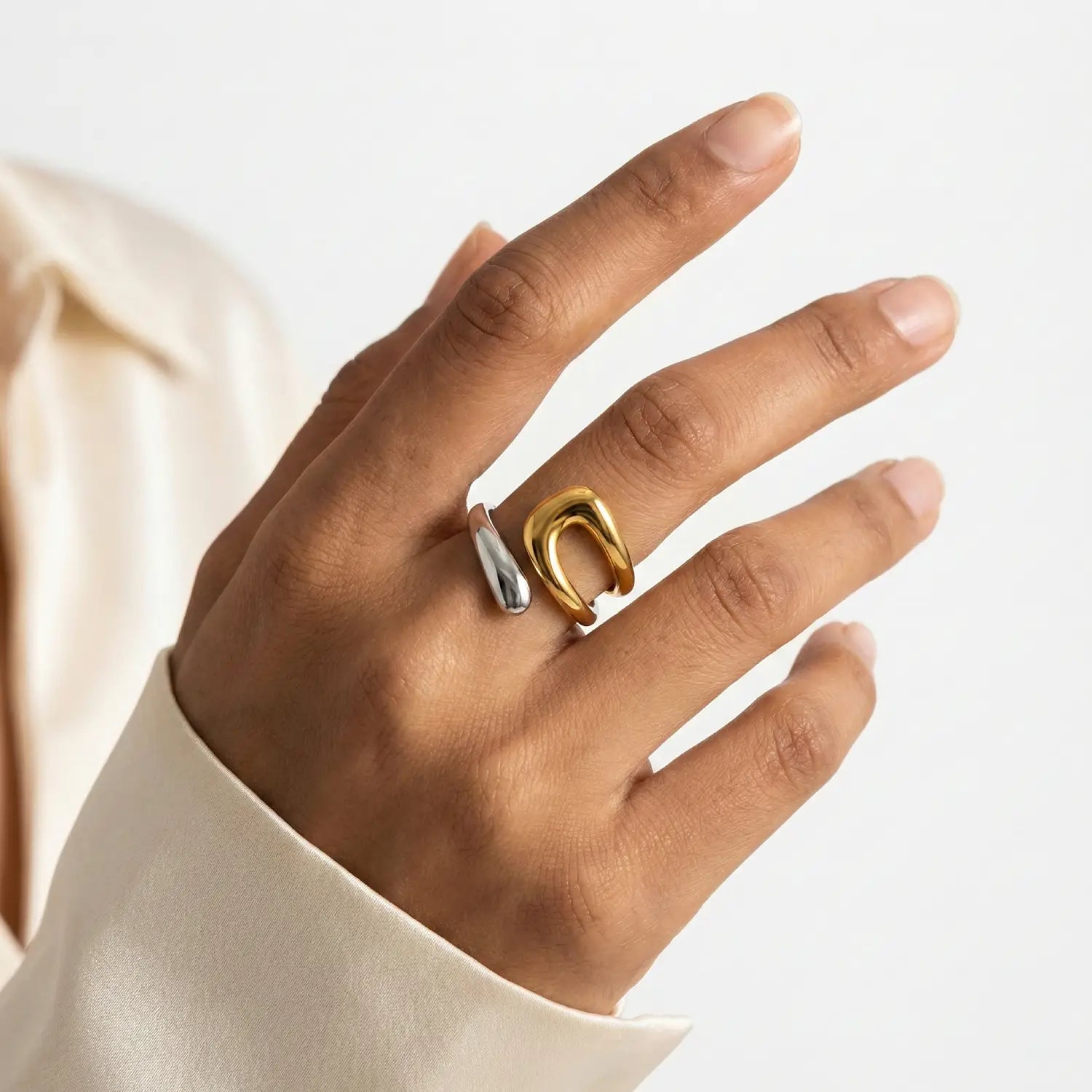 Hand wearing a gold and silver ring on a plain background